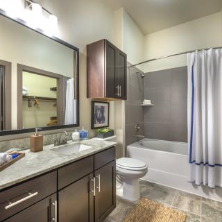 A modern bathroom with a large mirror, dark wood cabinets, and a tiled shower area.