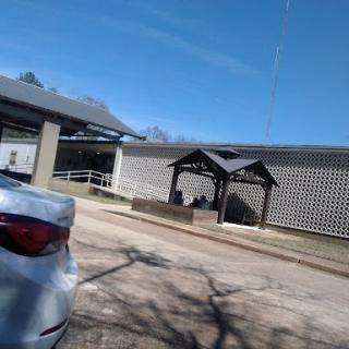 A view of a building with a shaded seating area and a parked car under a clear blue sky.