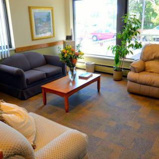 A cozy living room with sofas, an armchair, a coffee table with flowers, and large windows overlooking a view.
