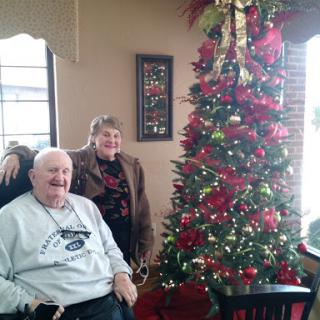 A cheerful couple poses by a beautifully decorated Christmas tree.