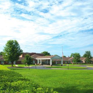 A spacious building surrounded by a large green lawn and trees under a partly cloudy sky.