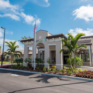 A view of a modern building with palm trees and well-maintained landscaping under a blue sky.