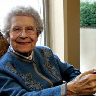 An elderly woman smiling warmly while seated comfortably indoors.