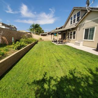 A sunny backyard with a well-maintained lawn and garden area beside a house.