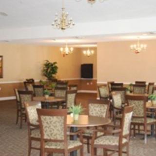 An empty dining room with multiple tables and chairs, decorated with chandeliers and a carpeted floor.