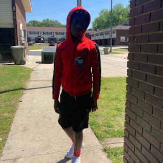 A person walking down the street on a sunny day, dressed in a red hoodie and shorts.