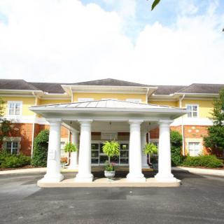 A symmetrical building entrance featuring prominent white columns and surrounded by greenery.