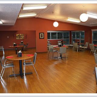 An empty cafeteria with neatly arranged tables and chairs on a wooden floor.