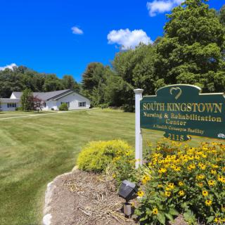 View of a sign and building surrounded by greenery and flowers under a clear blue sky.