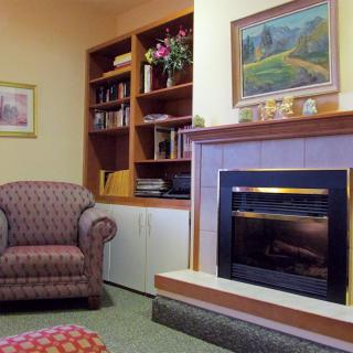A cozy living room featuring an armchair, a fireplace, and a bookshelf adorned with various items.