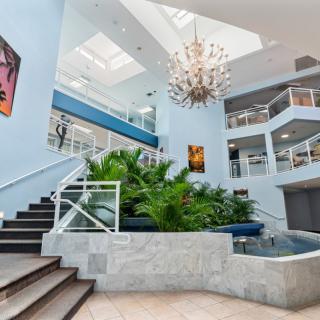 A modern atrium featuring a grand staircase, elegant chandelier, and lush indoor plants.
