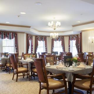 A well-lit dining area with elegant chandeliers, decorated windows, and neatly arranged tables and chairs.