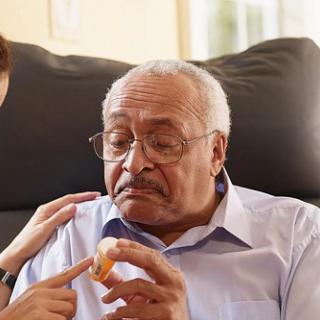 A caregiver assists an elderly man with food in a comfortable indoor setting.