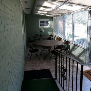 A sunlit indoor space with a round table and several chairs surrounded by large windows.