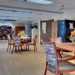 A spacious and well-lit dining area with multiple tables and chairs, featuring a bookshelf and decorative items.