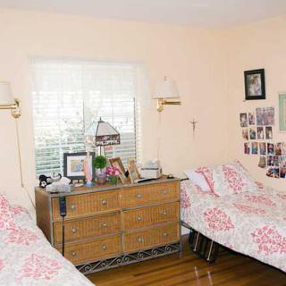 A cozy bedroom featuring twin beds with matching floral bedding, a dresser between them adorned with decor, and photos displayed on the wall.