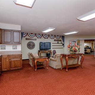 A cozy living room with a seating area, television, and decorative elements on a red carpeted floor.