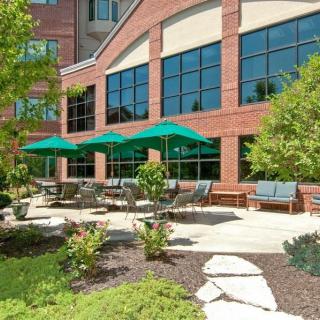 A modern building with a landscaped outdoor patio featuring seating and green umbrellas.