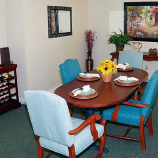 A cozy dining room with a wooden table set for four, surrounded by comfortable blue chairs, decorated with sunflowers and wall art.