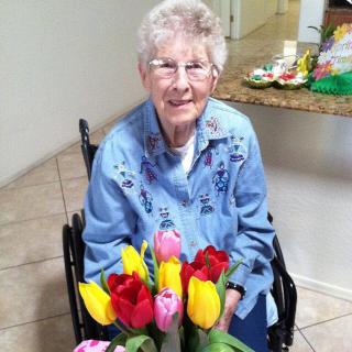 An elderly woman smiles while sitting in a wheelchair, holding a vibrant bouquet of tulips.