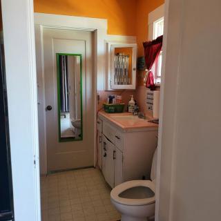 A small bathroom with orange walls, featuring a mirror, sink, and toilet.