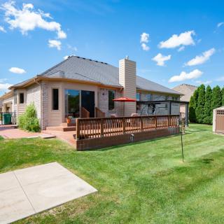 A suburban house with a spacious backyard, featuring a wooden deck and patio furniture on a sunny day.
