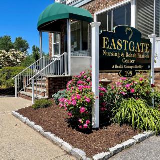 Entrance to Eastgate Nursing & Rehabilitation Center with flowers and signage.