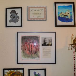 A collection of framed artwork and a certificate displayed on a gallery wall.