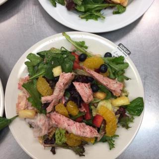 A colorful salad with mixed greens, fruit slices, and pieces of salmon.