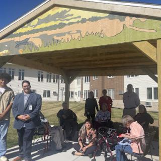 A community gathering under a beautifully painted shelter, showcasing diverse individuals engaged in conversation.