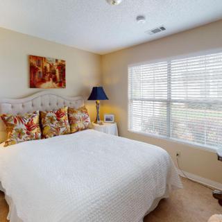 A cozy bedroom with a neatly made bed, decorative pillows, and a bedside lamp by the window.