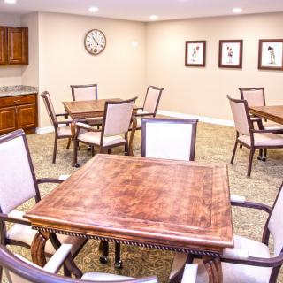 A cozy dining room with multiple wooden tables and upholstered chairs, featuring wall artwork and a clock.