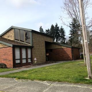 A modern residential building featuring a combination of brick and stone elements, set in a grassy landscape.