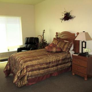 A cozy bedroom with a bed, nightstand, and armchair near the window.