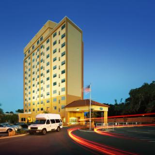 A tall hotel building illuminated at night with vehicles in the parking area.