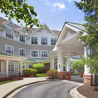 A picturesque entrance of a residential building with a landscaped driveway and surrounding greenery.