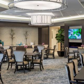 A well-lit dining room with elegant furniture and chandeliers, featuring tables and chairs arranged for dining.