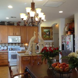 A beautifully decorated kitchen featuring wooden cabinets, a chandelier, peacock statues, and a dining table adorned with flowers and fruit bowls.