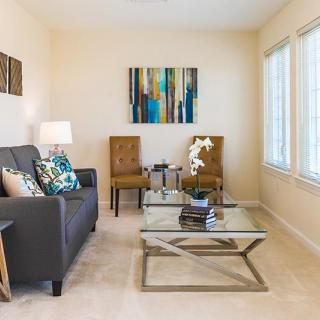 A modern living room with a sofa, two chairs, a glass coffee table, and decorative artwork on the wall.