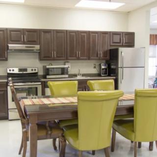 A modern kitchen with dark wooden cabinets, stainless steel appliances, and a dining area featuring green upholstered chairs around a wooden table.