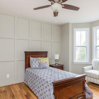 A cozy bedroom with a single wooden bed, an armchair by the window, and a ceiling fan.