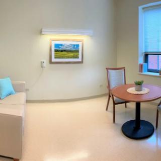 A modern hospital room featuring a sofa, table with chairs, and a framed artwork on the wall.