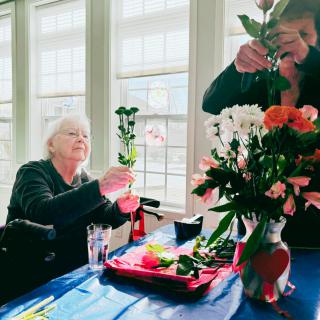 Two individuals engaging in a flower arranging activity at a table near the window.