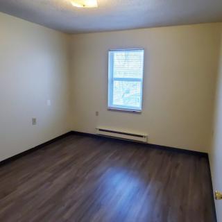 An empty room with a window, hardwood flooring, and neutral-colored walls.