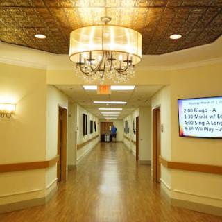 A well-lit hospital hallway featuring a chandelier and artwork along the walls.