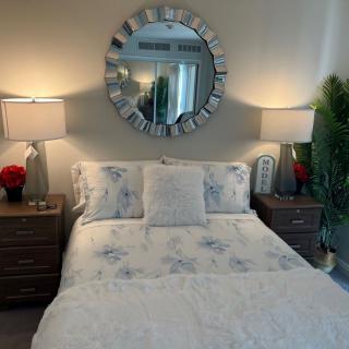 A cozy bedroom with a decorative mirror above the bed, flanked by nightstands and lamps, complemented by floral bedding and greenery.