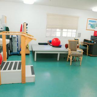 A well-equipped physical therapy room featuring exercise machines, balls, and a comfortable seating area.