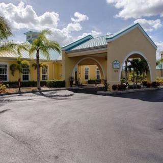 A tropical-style hotel entrance with palm trees under a sunny sky.