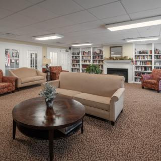A cozy living room with sofas, armchairs, a coffee table, bookshelves, and a fireplace.