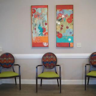 A waiting room with three chairs and colorful abstract artwork on the wall.